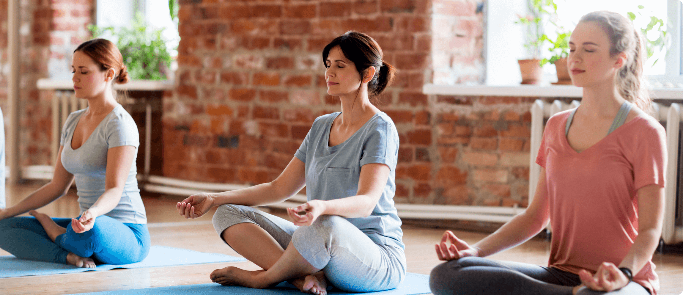 three-women-meditating-short Three women meditating within a room with brick walls and windows.