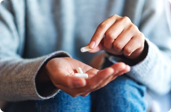 Image of a man's hands and clothed torso. Hands are holding nutritional supplement pills.