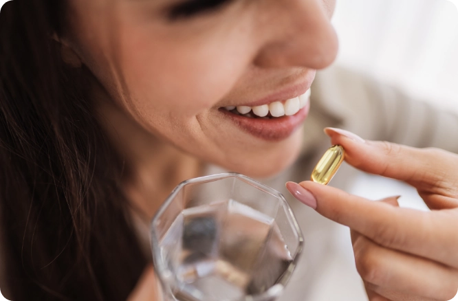 Close up image of woman's face and hands, one hand is holding a vitamin and the other hand is holding a glass of water.