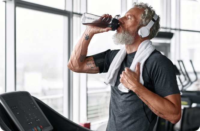 Man on treadmill with towel around neck and drinking from a water bottle.