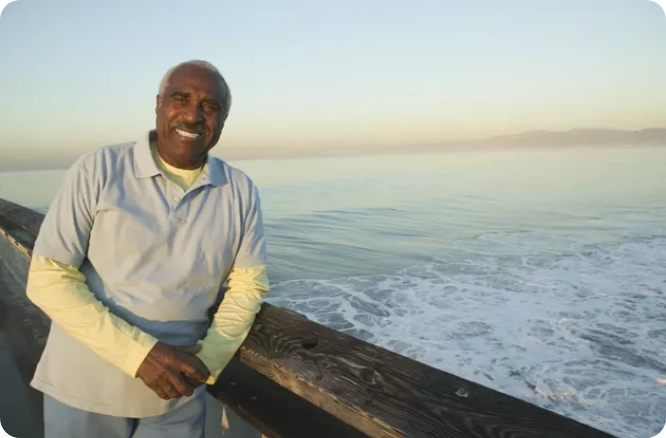 Man standing and resting against pier with ocean in the background.