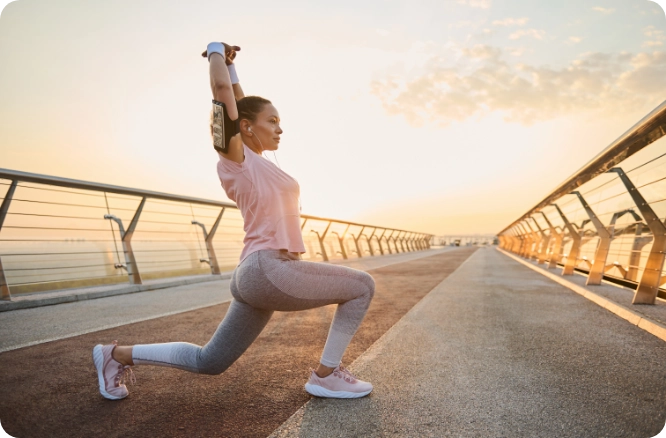 Woman in running clothes stretching on the roadside with dawn sun rising in background.