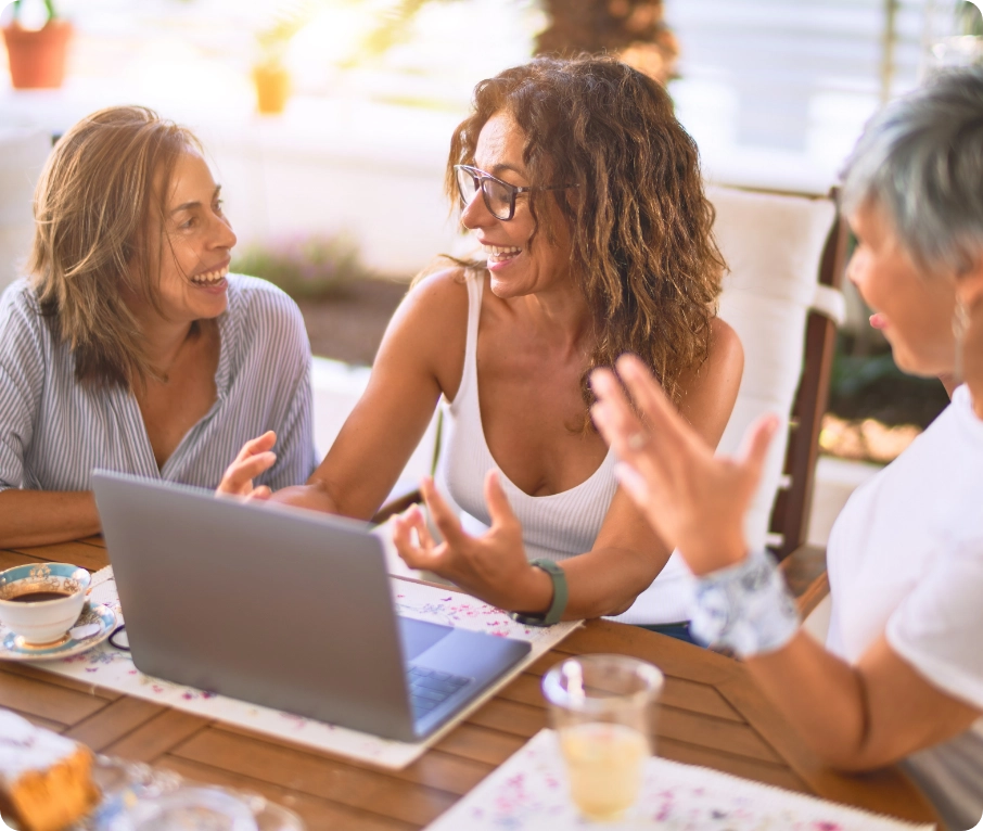 Woman using a laptop and talking to two other women on her right and left side.