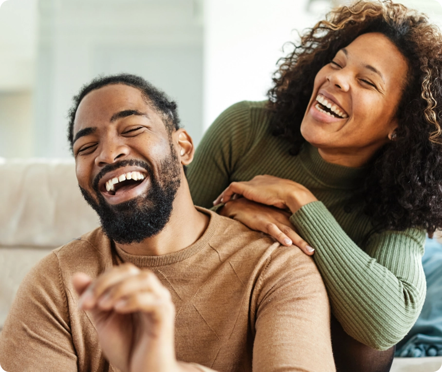 Male and female couple sitting and laughing together in a living room.
