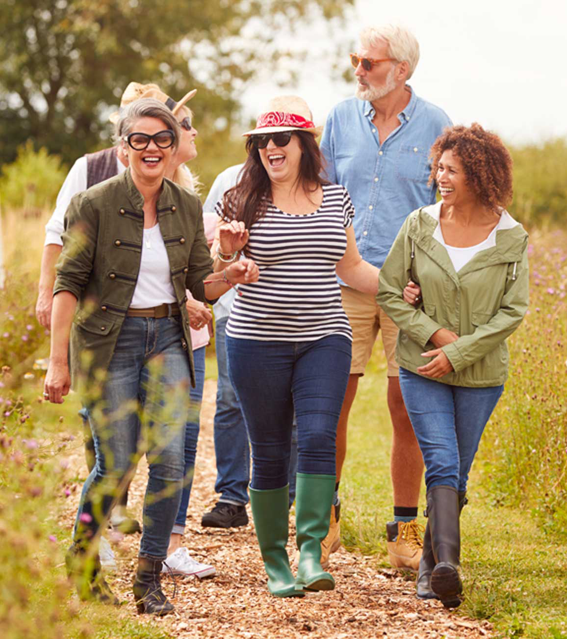Group of adults walking together outdoors on a nature trail, representing wellness and an active lifestyle across adulthood.
