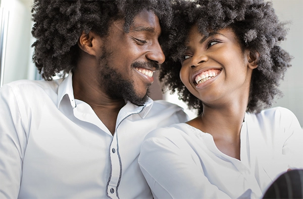 Male and female couple sitting side by side, smiling, and looking at each other