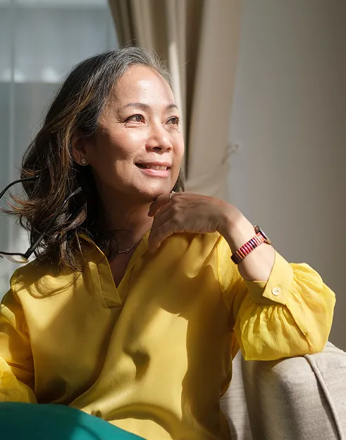 healthy-aging-wellness-woman-natural-light Smiling woman sitting in natural light, representing healthy aging and wellness.
